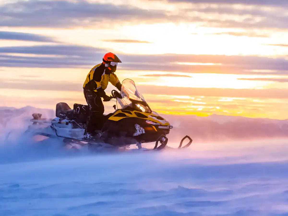 Snowmobilier riding at sunset