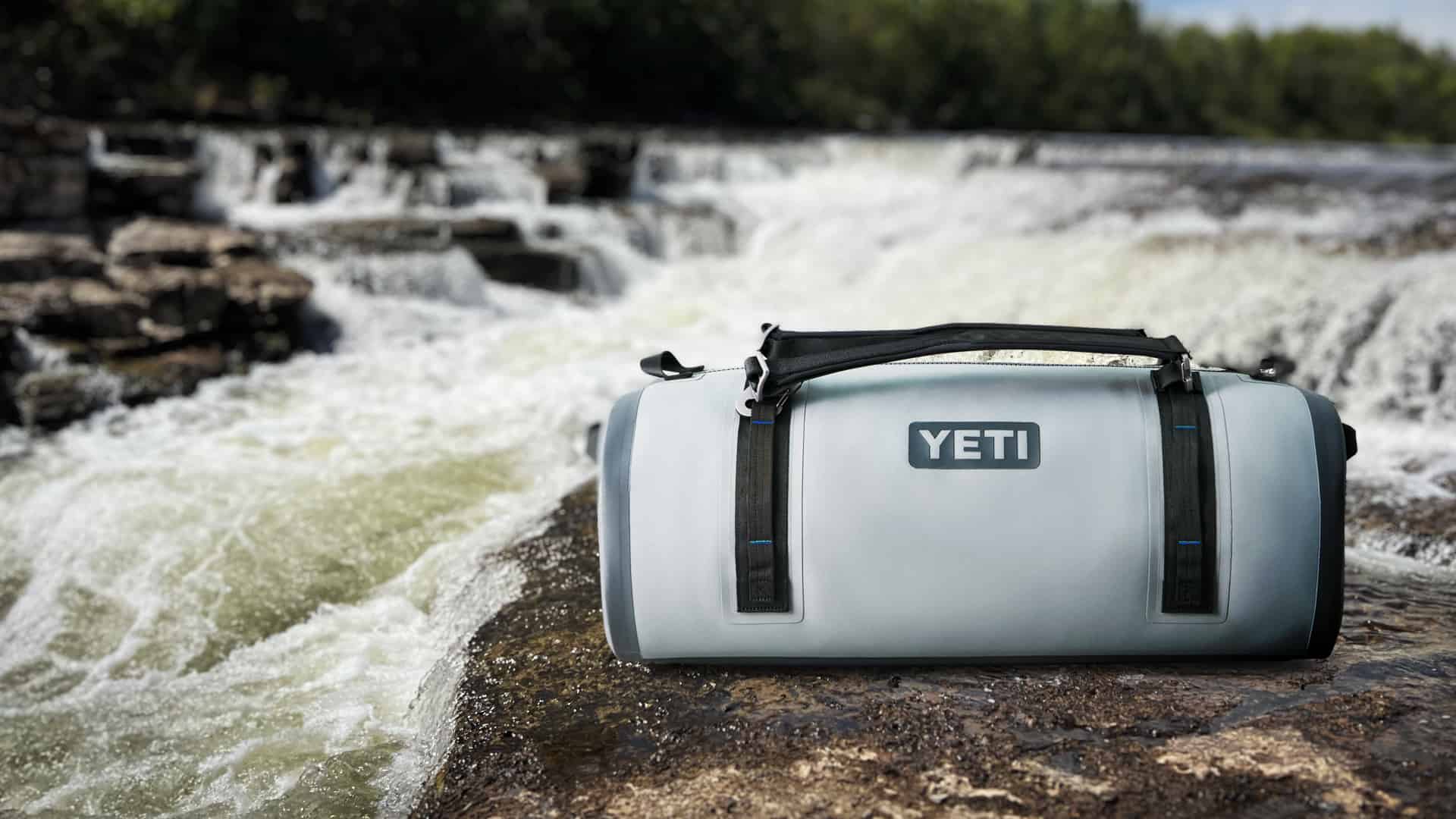 Yeti Panga 75 waterproof duffle on a rock beside a waterfall