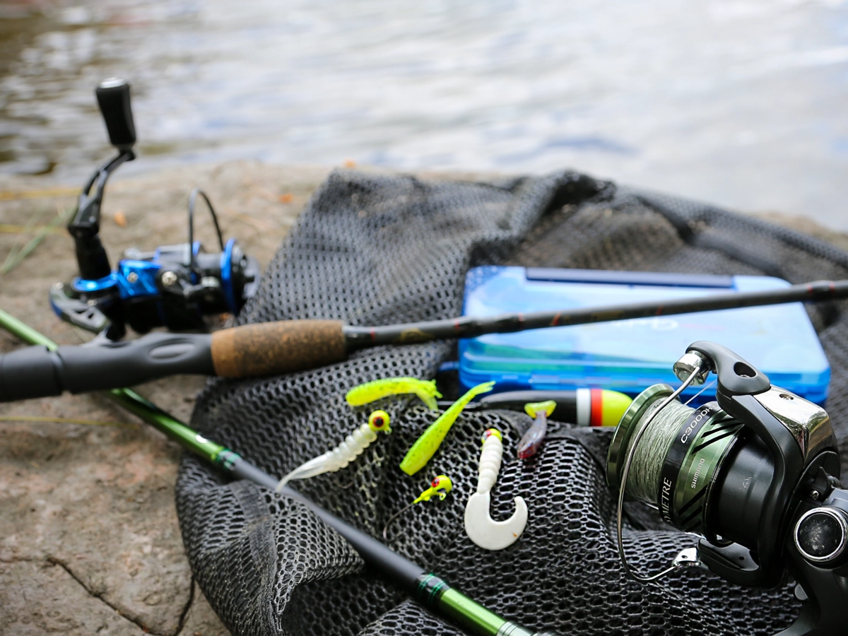 Crappie fishing gear essentials laid out on a rock by a serene lake, including jigs, rods, lures, and a fishing net.