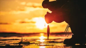 As the sun sets, an angler is wearing thick layers of clothing to keep warm while ice fishing