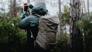 A women taking photos while hiking with the YETI Ranchero Backpack in dark cape taupe