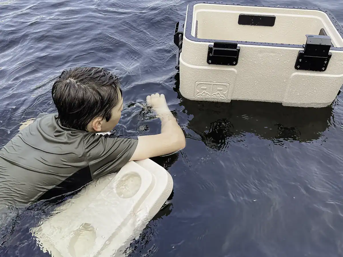 young man floating on the Rugged Road cooler lid in the lake