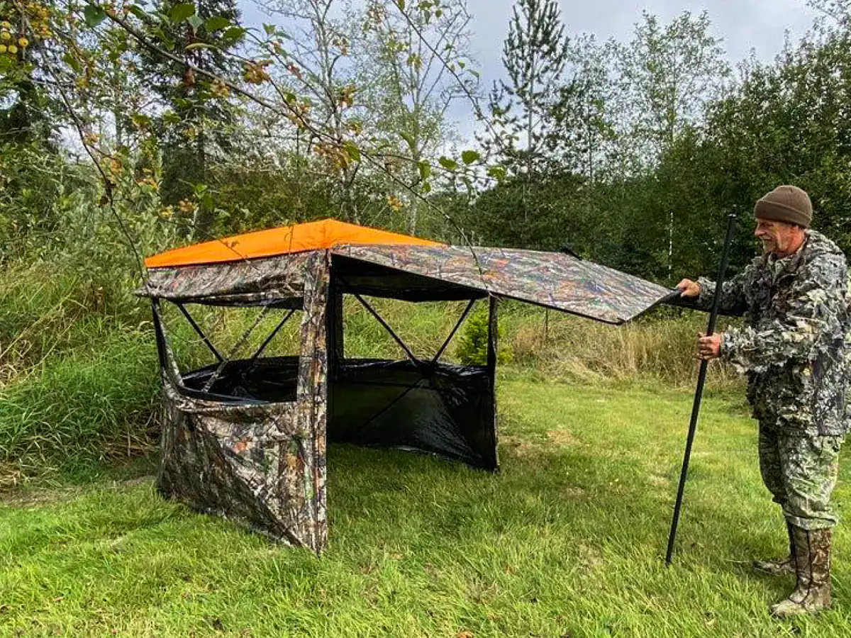 Camouflage hunting blind setup in outdoor wilderness with hunter opening the FlipGuard hunting blind door