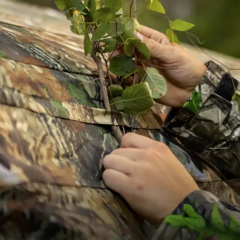 Hunter using the brush loops to camouflage the all weather TideWe FlipGuard 270 ground blind